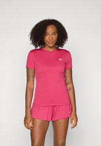 Conjunto de roupa desportiva ajustada em rosa brilhante. Top de manga curta com decote redondo e logotipo; calções combinando com um corte relaxado e pregas subtis.