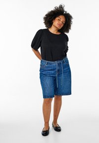 Top corto a maniche corte nero in tessuto testurizzato, abbinato a pantaloni bermuda in denim blu con cordoncino e tasche. Scarpe nere flat.
