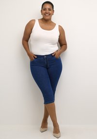 Jeans capri in denim blu con vestibilità slim, dotati di chiusura a bottone e tasche. Abbinati a un top bianco e tacchi beige.