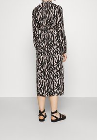 Svart och rosa mönstrad midiklänning med långa ärmar och knytning i midjan, tillverkad av ett lätt material. Sandalerna har svarta remmar och spänne.