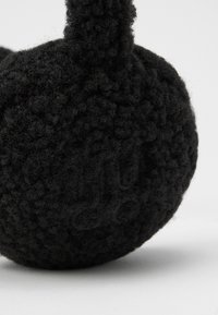 Casque noir texturé de forme ronde, fabriqué en matériau doux. La surface présente un logo en relief subtil.