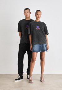 Charcoal gray oversized t-shirts with circular graphic and text, paired with a denim skirt, black sneakers, and silver heeled sandals.