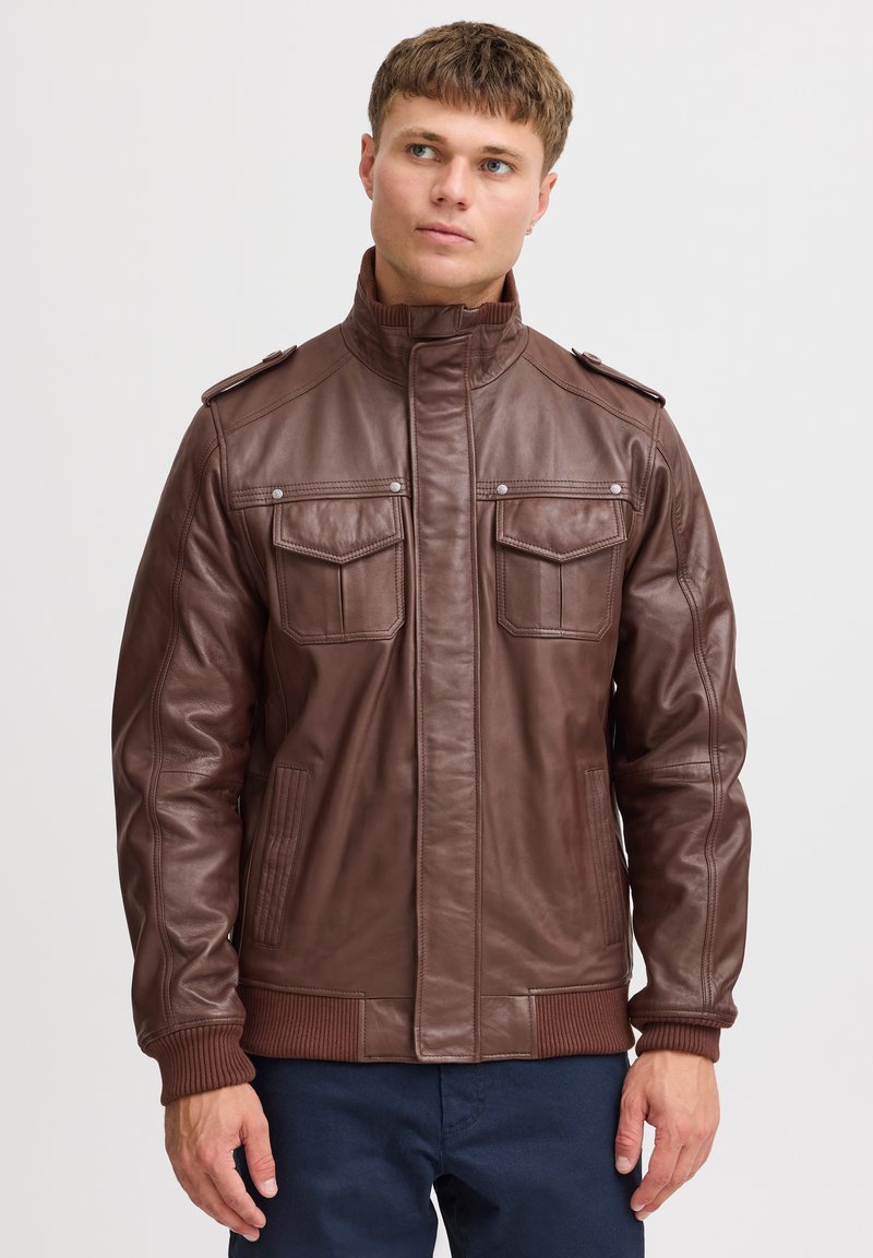 Veste en cuir marron avec un col montant, deux poches avant, des pattes d'épaule et des poignets côtelés. Texture lisse et design structuré.