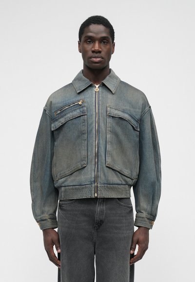 Denim jacket, light blue with a slightly faded finish, features two chest pockets and a front zipper. It has a structured collar and cuff details.
