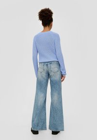 Hellblauer gestrickter Pullover mit rundem Halsausschnitt, kombiniert mit weit geschnittenen hellen Jeans. Das Outfit hat eine entspannte Passform und gerippte Textur.