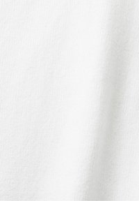 Gros plan sur un tissu blanc tricoté doux montrant une texture détaillée et des ombres subtiles à la surface.