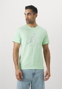 T-shirt di cotone verde chiaro con un logo Jumpman argentato lucido e la scritta "SPORTS" sottostante. Maniche corte e design a girocollo.