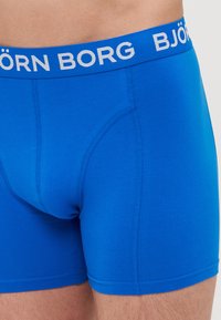 Kék boxernadrág fehér gumis derékkal, amelyen a "BJÖRN BORG" logó található. Simaságával és testhezálló kialakításával, oldalsó varrásokkal rendelkezik.