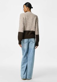 Pull en tricot avec un col rond, section supérieure beige, section inférieure marron foncé, et poignets et ourlet côtelés ; assorti avec un jean large bleu clair.