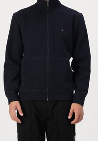 Sudadera con cremallera en color navy, hecha de tela suave, con un cuello alto, bolsillos frontales y un pequeño logo en la parte izquierda del pecho.