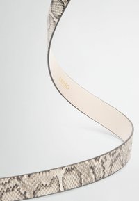 Ceinture à motif python avec un intérieur lisse, présentant une forme étroite et un bord noir contrastant. Logo doré "LIU JO" visible.