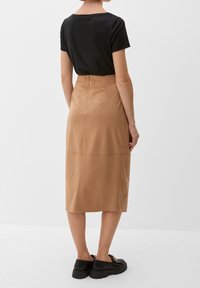 T-shirt noir à manches courtes associé à une jupe tan au genou, présentant une texture douce, avec des chaussures noires visibles en bas.
