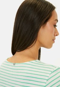 Gestreepte trui in wit en mintgroen met een ronde hals. Bevat een subtiele metallic detaile aan de achterkant van de nek. Zachte textuur.