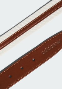 Brunt läderrem med vit vävd tygsektion, med guldsömmar och präglad Adidas-logotyp. Inkluderar justeringshål.