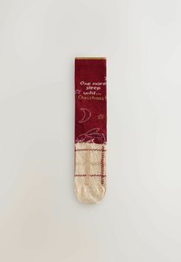 Röd och krämfärgad feststrumpa med gula accenter, som har texten "En sömn kvar till jul" och ett mönster med stjärnor och en kanin.