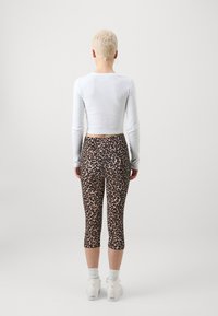 Dugi rukav bijeli rebrasti crop top u kombinaciji s tajicama do polovice lista s leopardskim uzorkom i bijelim tenisicama s teksturiranom đonom.