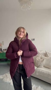 Giubbotto imbottito color borgogna con cappuccio; trama gonfia, chiusura con zip e tasche laterali. Indossato sopra una maglia bianca, abbinato a pantaloni neri.