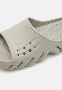 Grey slide sandal made of lightweight rubber with a textured surface, open toe, and ventilation holes for breathability. Features wavy design.