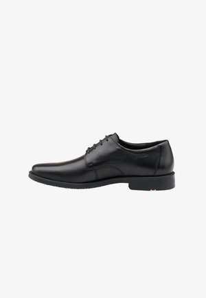 Chaussure de ville en cuir noir au design épuré, à bout pointu, avec un système de laçage et une semelle en caoutchouc texturée et basse. Accent rouge sur le talon.