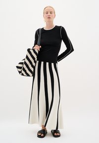 Melna garām piedurknēm topa ar baltām akcentiem, apvienota ar melnbaltu svītrainu maxi svārku. Melnas sandales un atbilstoša svītraina somiņa.