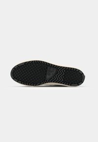 Semelle extérieure en caoutchouc noir avec un motif de grip texturé, dotée d'une semelle intermédiaire beige et d'un design à bout rond, avec des couleurs contrastées tout au long.