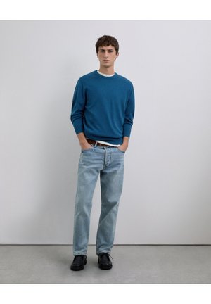 Suéter azul de manga larga con cuello redondo, combinado con jeans de pierna recta de color azul claro y zapatos negros. Diseño sencillo, sin estampados.