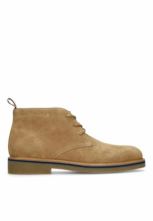 Tan suede ankle boot with three eyelet laces, blue-striped sole, and pull tab at the back.