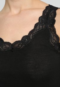 Top a canottiera nera a coste con un delicato bordo in pizzo lungo il colletto e le bretelle. Il tessuto sembra morbido e leggermente testurizzato.