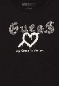 Mustar T-särk, millel on "GUESS" studeeritud gooti fondis, tilkuv valge süda ja tekst all, mis loeb "mu armastus on sinu jaoks."
