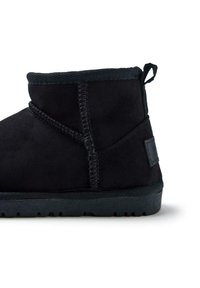 Stivale alla caviglia in suede nero con dettagli cuciti, una silhouette arrotondata e una suola in gomma testurizzata. Presenta un tassello sul retro.