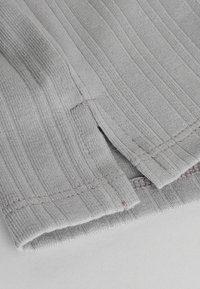 Tissu en coton gris avec une texture côtelée verticale, présentant des bords finement finis et un détail de couture subtil, disposé à plat sur une surface blanche.