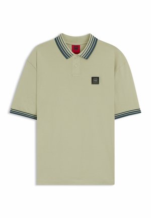 Pale green polo shirt with a two-tone collar featuring dark stripes, short sleeves, and a black logo patch on the chest.