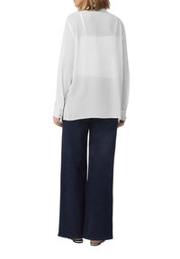 Witte, sheer blouse met lange mouwen en een relaxte pasvorm. Gecombineerd met donkerblauwe wijde spijkerbroeken. Voorzien van knoopmanchetten en zijslits.