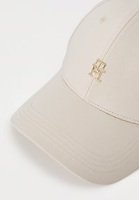 Casquette de baseball beige en tissu texturé, avec un accent logo doré à l'avant et une couture distincte le long de la visière.