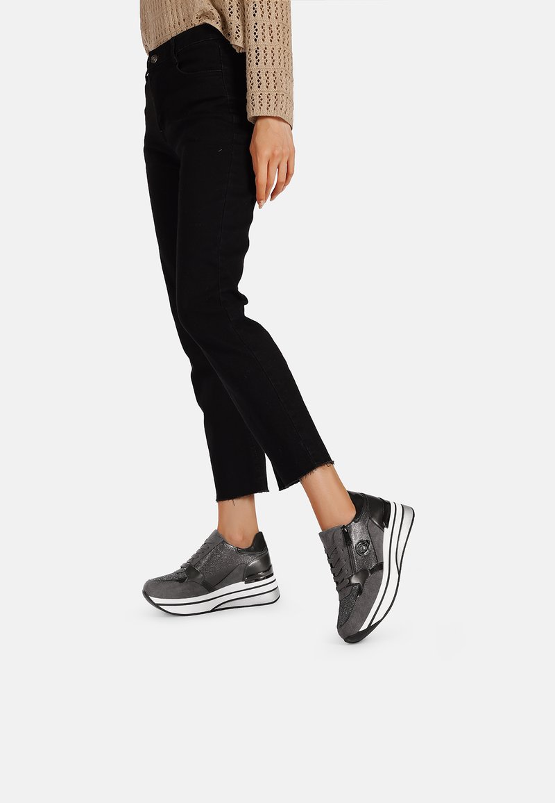 Scarpe da ginnastica grigie con una parte superiore testurizzata, design con stringhe e dettagli bianchi nella suola intermedia. Indossate con jeans neri a vita alta.