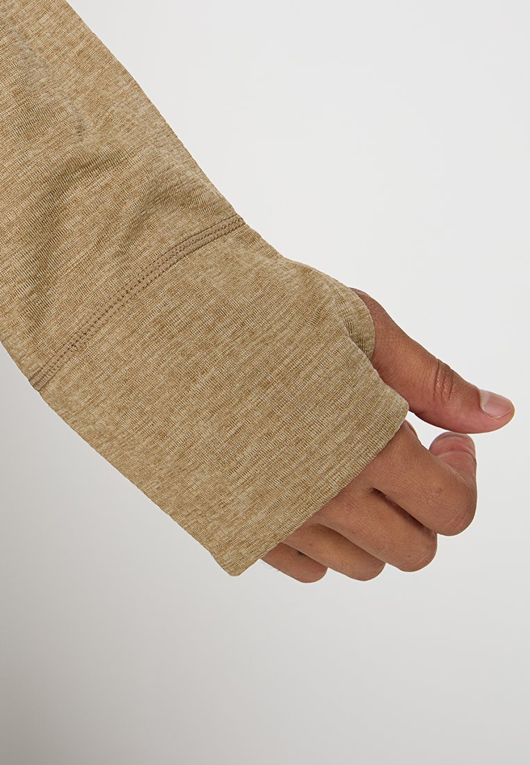 Una mano parzialmente coperta da una manica con foro per il pollice di un marrone chiaro su uno sfondo chiaro.