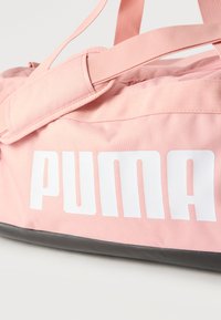 Ροζ αθλητική τσάντα duffel της Puma με λευκό λογότυπο, μαλακό λουρί ώμου και μαύρη βάση σε λευκό φόντο.