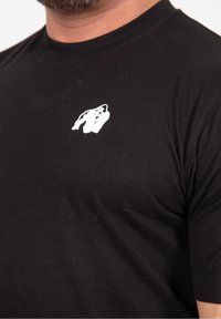 Černé bavlněné tričko s bílou grafikou gorily na levé straně hrudníku. Krátké rukávy a klasický kulatý výstřih.