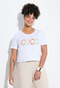Camiseta blanca de manga corta con letras florales "Coco", combinada con pantalones claros de lunares. Material de algodón suave.