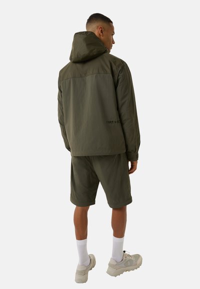 Olive green lightweight jacket with a hood, paired with matching shorts. Features a logo on the back and textured fabric for breathability.