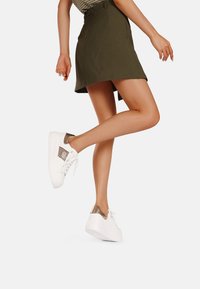 Sneaker bianche con accenti dorati metallici sul tallone e sul lato, caratterizzate da un pannello testurizzato. Il design è minimalista con una suola piatta.