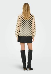 Gennemsigtig bluse med polka dot i beige med sorte prikker, med lange, puffede ærmer. Kombineret med en sort læder miniskørt og knæhøje støvler.