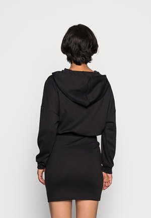 Robe à capuche noire avec manches longues et capuche. Fabriquée en tissu doux, elle présente une silhouette ajustée et une texture sans coutures.
