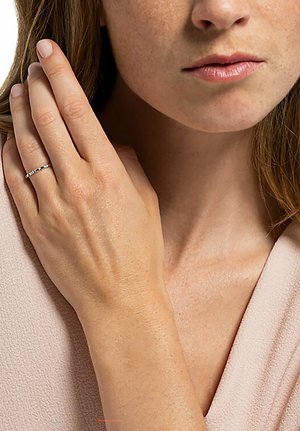 Silberring mit kleinen rechteckigen Akzentsteinen, schmale Band, glatte Oberfläche. Hand ruht sanft nahe dem Gesicht und zeigt ein dezentes, elegantes Design.