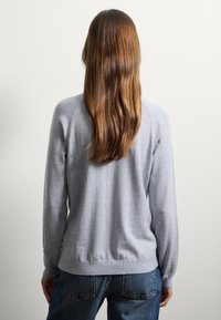 Pull gris à manches longues, avec un ourlet côtelé, texture douce, porté avec un jean taille haute bleu. Vue de dos sur un fond uni.