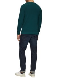 Emeraldgroen gebreid sweater met ronde halslijn, geribbelde boorden en zoom, gecombineerd met donkere spijkerbroek en witte sneakers.