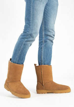 Botas de tobillo de ante marrón con un suave forro interior, que cuentan con una suela de goma plana, un diseño cosido y una tira en la parte posterior.
