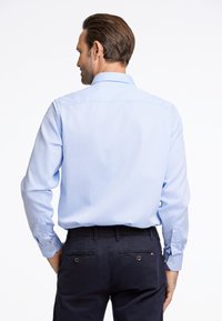 Lichtblauw overhemd met lange mouwen, een subtiele textuur, getailleerd design en knoopmanchetten, gecombineerd met donkere broek met achterzakken.