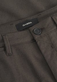 Bruine Gabba-broek met een textuurstof, een zwarte knoopsluiting en een label op de tailleband genaaid. Rechte pijpen, minimalistische details.