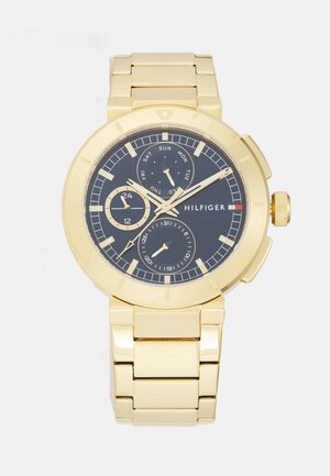 Gold-tone stainless steel watch with a dark blue dial, chronograph features, three sub-dials, and a textured crown. Silver accents on the face.